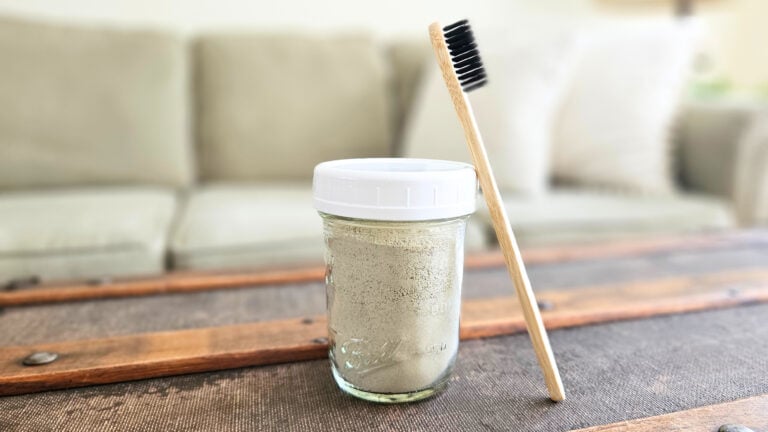 Half pint mason jar of homemade tooth brushing powder with a bamboo toothbrush.