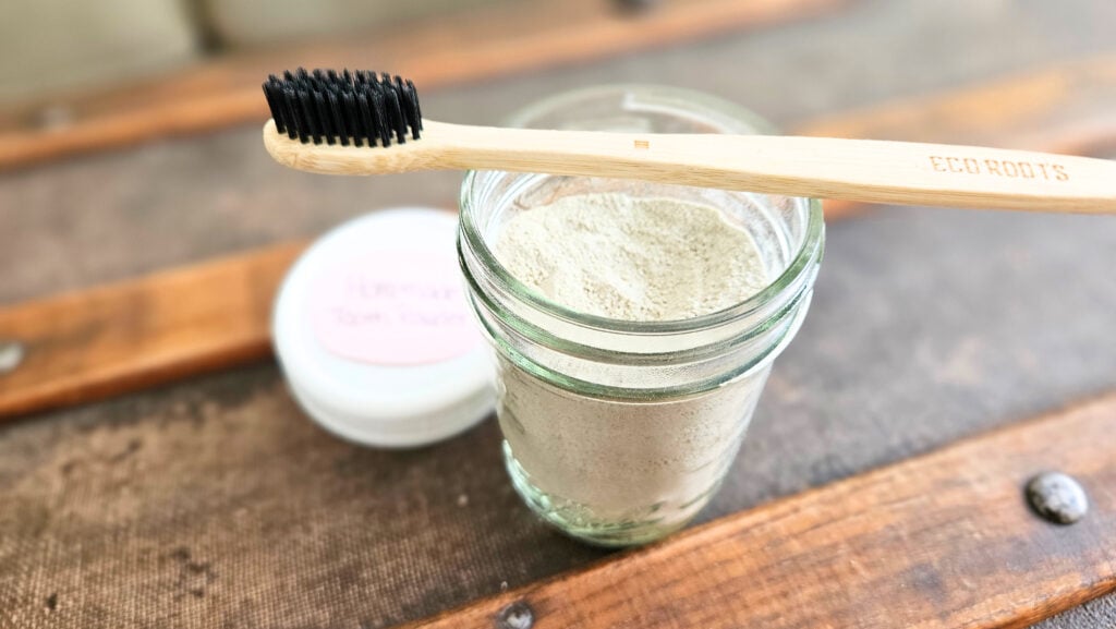 Half pint mason jar of homemade tooth brushing powder with a bamboo toothbrush.
