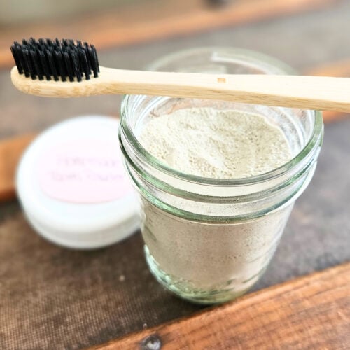 Half pint mason jar of homemade tooth brushing powder with a bamboo toothbrush.
